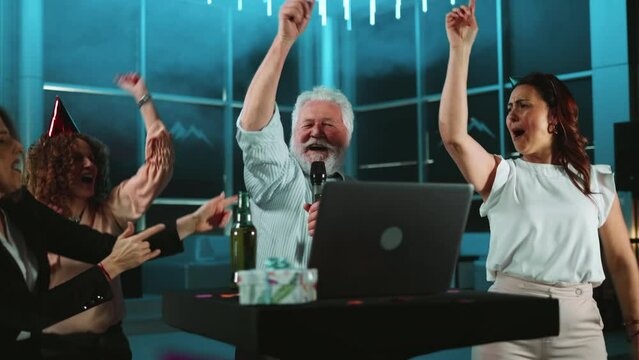 Slowmo of  happy business friends singing into a microphone while doing karaoke at a birthday party in a nightclub