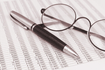 Black round eyeglasses in metallic frame with pen on documents with numbers.