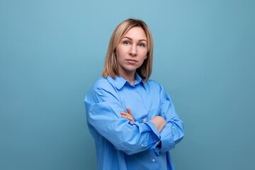 serious european blond woman folded her hands in front of her on a blue background with copyspace