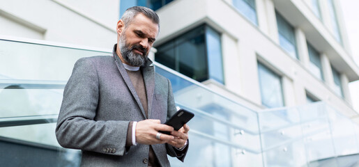 mature adult male financier with gray hair and a beard with a phone in his hands on the background...