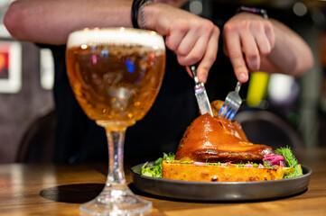 man cuts a pork knuckle with a knife and fork