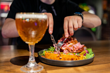 man cuts a pork knuckle with a knife and fork