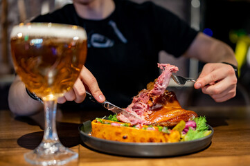 man cuts a pork knuckle with a knife and fork