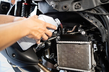 Hands of motorcycle mechanic filling cooling system with engine coolant,pour coolant after...