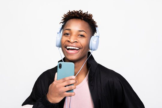Attractive cheerful afro american man in casual stylish outfit clothes smiling wearing wireless purple headphones holding cell phone smartphone near mouth singing in phone like microphone.