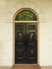 old wooden black door with arched frame on cream wall