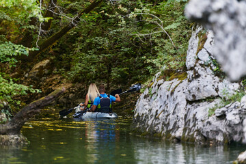 A young couple enjoying an idyllic kayak ride in the middle of a beautiful river surrounded by forest greenery