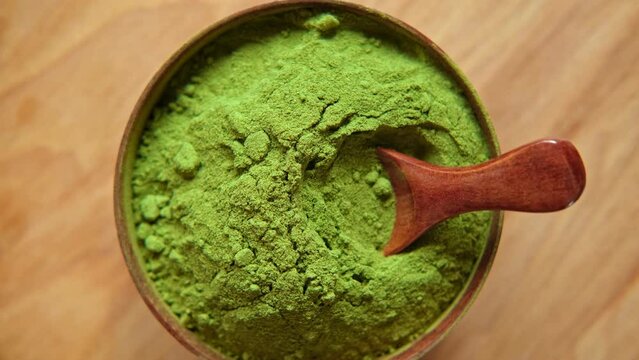 Powdered matcha tea, Wooden spoon in a bowl spinning on natural background. Matcha powder. Top view, Closeup. Finely ground green powder. Japanese culture. Healthy eating with high antioxidants.