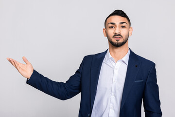 Happy serious turkish man handsome guy in smart ellegant suit costume and white shirt pointing at something talking buisnessman stands over grey background in studio isolated.