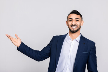 Middle eastern young attractive man buisnessman with beard looking at camera smiling pointing at something talking at camera standing over grey background.