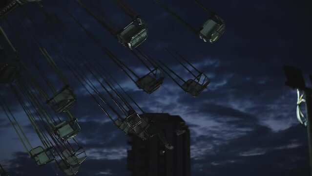 A young woman rides alone late at night on a carousel. Mountains behind, slow motion.