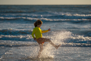 Obraz premium Active little kid running along sea beach during leisure sport activity. Sporty kid running in nature. Child run at seaside. Kids running on beach. Summer vacation. Happy childhood.