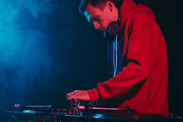 Hip hop DJ mixing vinyl records on stage. Cool young disc jockey playing music in dark night club