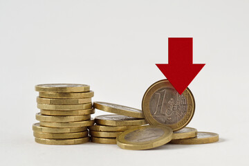 Piles of euro coins with red decreasing arrow on white background - Concept of decrease in euro value and loss of money
