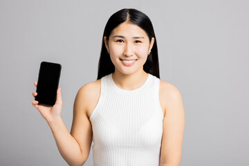 Young asian japanese korean woman on grey background in studio isolated wearing white t-shirt holding new cellphone smertphone looking pointing at copyspace black screen on phone.