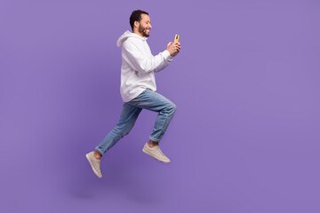 Fototapeta na wymiar Full body length cadre of young hispanic guy running with telephone texting his friends before meet isolated on violet color background