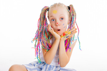 Portrait of delighted schoolgirl with colorful stylish pigtails shows surprised emotions at camera smiling having hands full of colorful paints holding near face sitting on white background isolated.