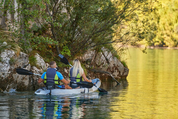 A young couple enjoying an idyllic kayak ride in the middle of a beautiful river surrounded by forest greenery