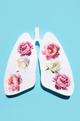 Paper silhouette of anatomical lungs with flowers inside on a blue background. The concept of healthy breathing. Vertical image.