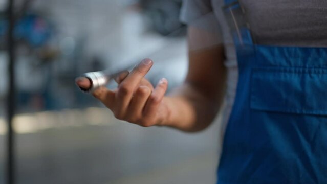 Closeup wrench spinning on male finger in slow motion indoors. Closeup unrecognizable young Caucasian man in overalls with tool at car service station