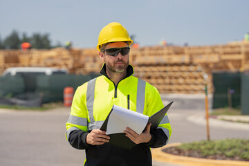 Construction worker at house under construction. Male builder construction worker a job site. Portrait of builder engineer worker in helmet at american house building site background.