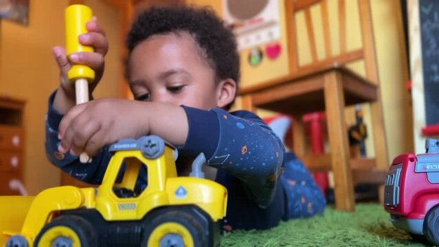 Scene of a three-year-old  black toddler playing at home to fix his toys laying on a green rug. He is wearing a blue pyijamas