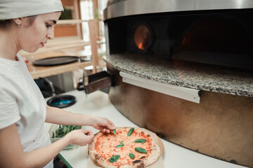 Cook garnishing a pizza with basil in a restaurant