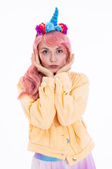 Beautiful thoughtful girl holding hands near face wearing unicorn headband and pink wig posing for camera in yellow denim jacket standing on white background in studio isolated fashionable shooting.