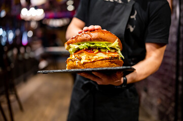waiter hands hold a plate with a very big cheeseburger in pub