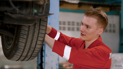 Caucasian male mechanic inspecting car wheels that has been damaged by accident Do repairs to customers' cars that come to use the service. Let's come back to use normally. in the garage