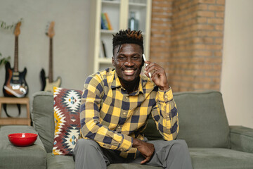 Handsome African man talking to the phone while sitting on a sofa in cozy living room. Young man using the phone.