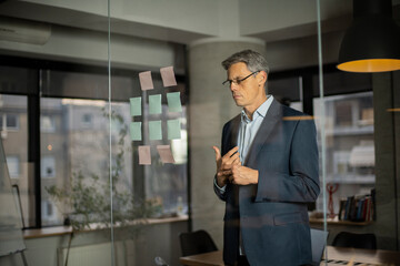 Portrait of successful businessman in office. Man writing ideas on colorful stickers on glass wall.