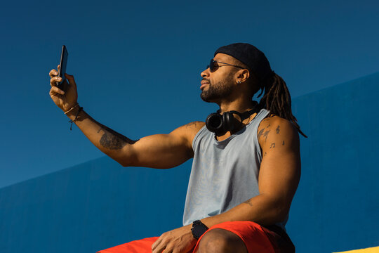 Black man taking selfie photo outside. Urban man posing with roller skates.