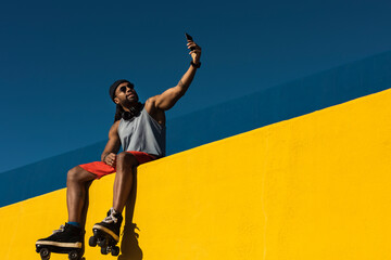 Black man taking selfie photo outside. Urban man posing with roller skates.