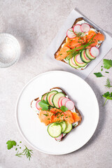 Healthy Scandinavian and Baltic  snack, lunch. Summer menu, Denmark. Smorrebrod, toasted bread with rye bread, salmon,curd cheese with herbs, green wild onion, cucumber and radish and microgreens