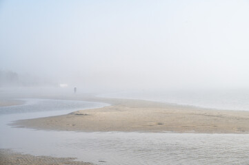 Fog on Baltic sea coastline at spring. Moody weather, mist. Person standing in distance