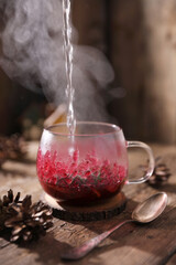 Tea with herbs, berries and fruits in a transparent cup on a wooden background