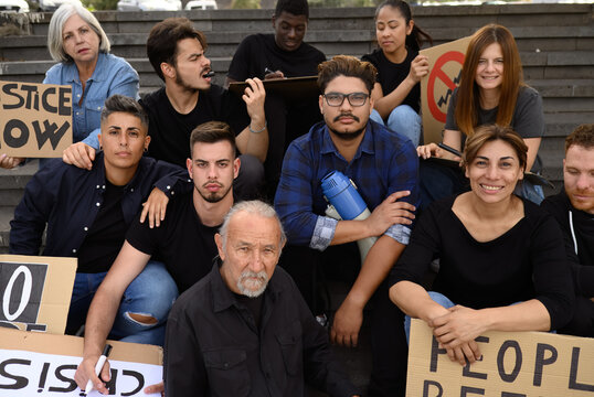 Group of multiethnic protesters in casual clothes with carton placards sitting on stairs on street before strike