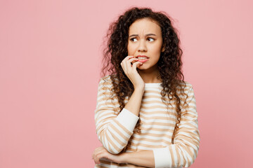 Young mistaken puzzled confused dissatisfied woman of African American ethnicity she wear light casual clothes look aside biting nails fingers isolated on plain pastel pink background studio portrait.