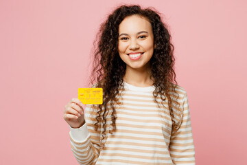 Young surprised shocked happy fun woman of African American ethnicity she wear light casual clothes hold in hand mock up of credit bank card isolated on plain pastel pink background studio portrait.