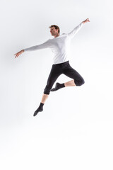 Fototapeta na wymiar Professional Caucasian Handsome Young Athlete Man Posing in Flying Ballet Pose with Lifted Hands in White Shirt On White.