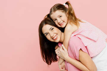 Happy woman wear casual clothes with child kid girl 6-7 years old. Mother, giving piggyback ride to joyful daughter, sitting on back isolated on plain pastel pink background. Family parent day concept