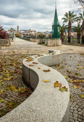 Obraz premium Curved stone bench leading the eye towards the entrance to the medieval bridge of Mirandela in Portugal on an autumn day.