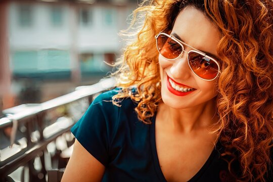 smiling young moroccan woman, with curly brown hair, sitting in an outdoor cafe in Mainz, wearing sunglasses