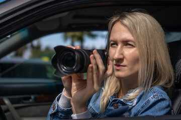 Young blonde woman takes pictures sitting in a car. Concept of journalism, detective, papparation