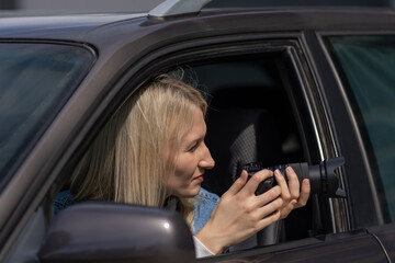 Obraz na płótnie Canvas Paparazzi woman or girl sits in her car and takes pictures of famous person. Spy with camera in car. Private detective or paparazzi journalist sitting inside car, taking pictures with camera.