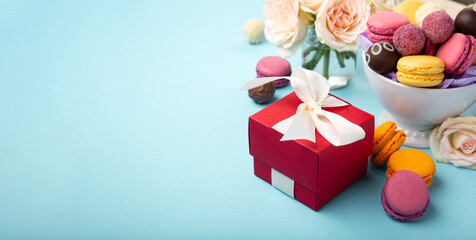 Macaroons, Gift Box, Rose Flowers and Chocolate Candies on Blue Background. Spring Presents Concept