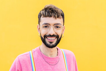 Smiling portrait of young cheerful bearded gay man looking at camera over yellow background. LGTBQ...