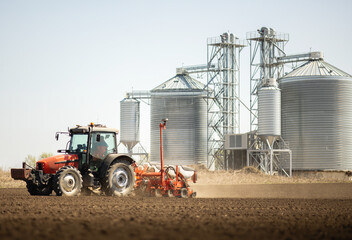 Tractor and seeder for sowing cornin. Silo in background