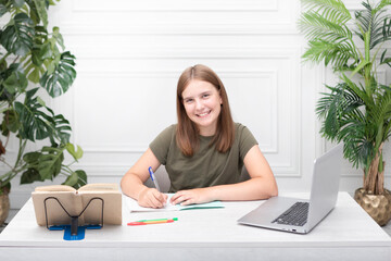 Portrait of lovely school girl sitting at the table and studying online. Distance education and preparation for school concept